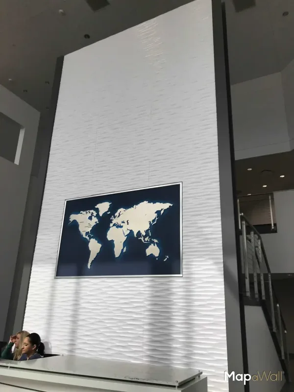 Magnetic MapaWall Stainless Steel world map with country borders installed on a blue panel above an office reception